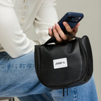 Person holding a black overnight toiletry bag in hand